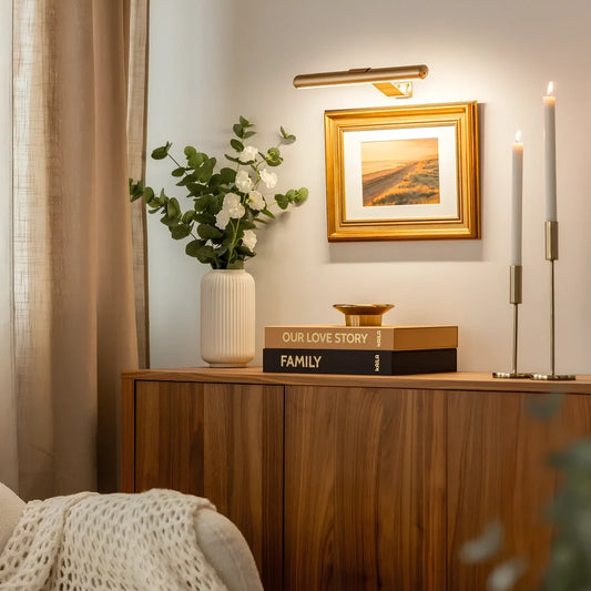 Lucía draadloze schilderijverlichting in goud boven een lijst in de woonkamer