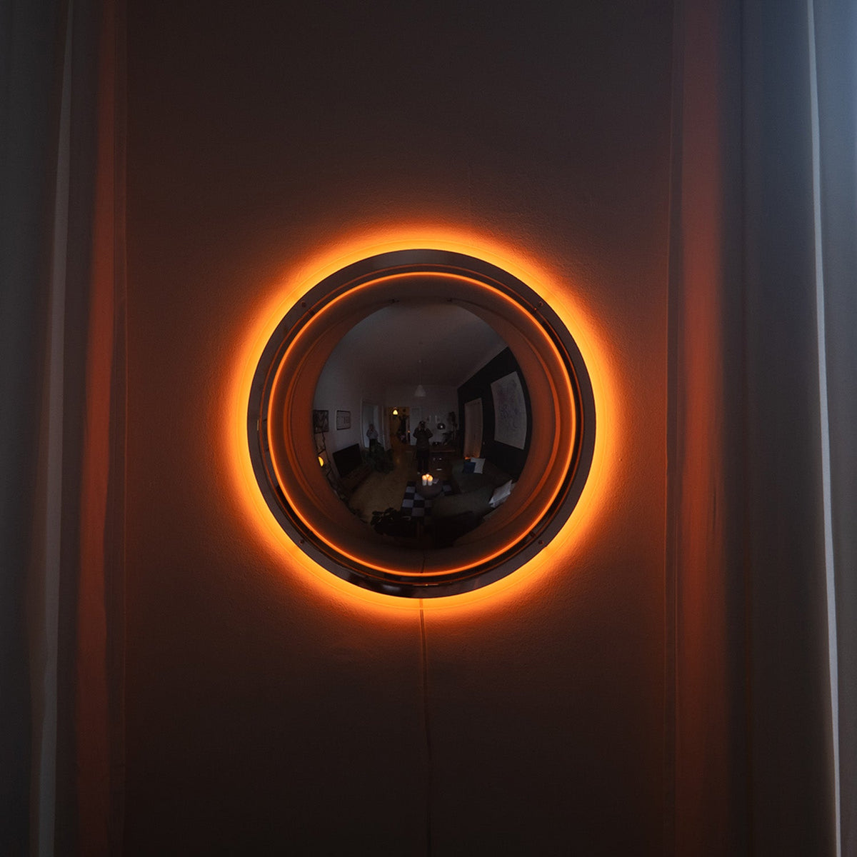 Lieve ronde spiegel wandlamp met warme halo-gloed aan donkere wand